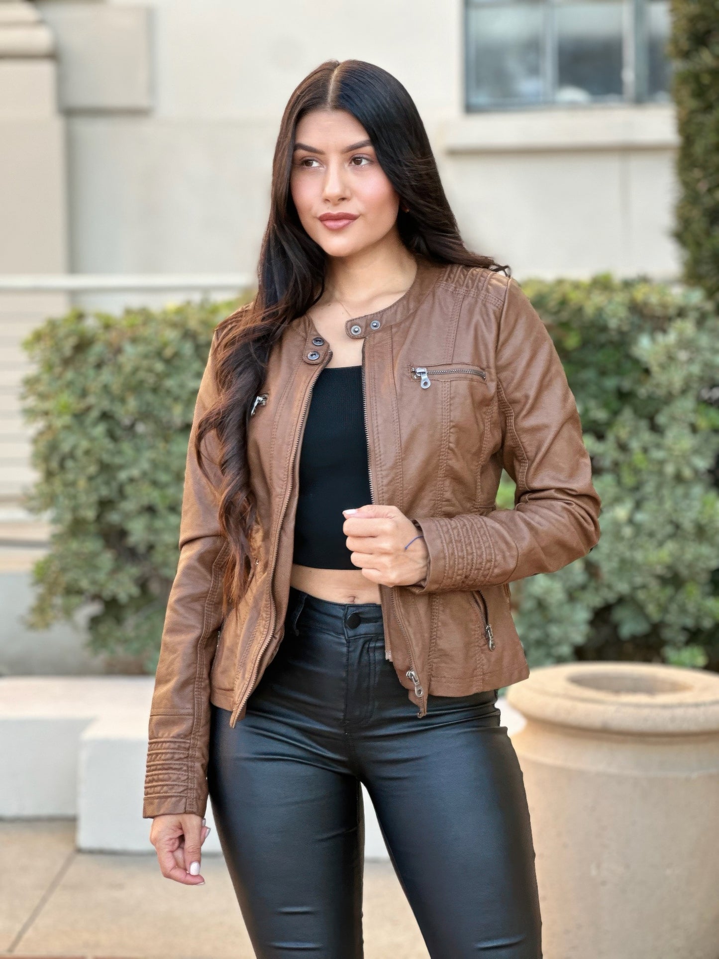 Woman wearing a brown leather jacket and black pants standing outdoors.
