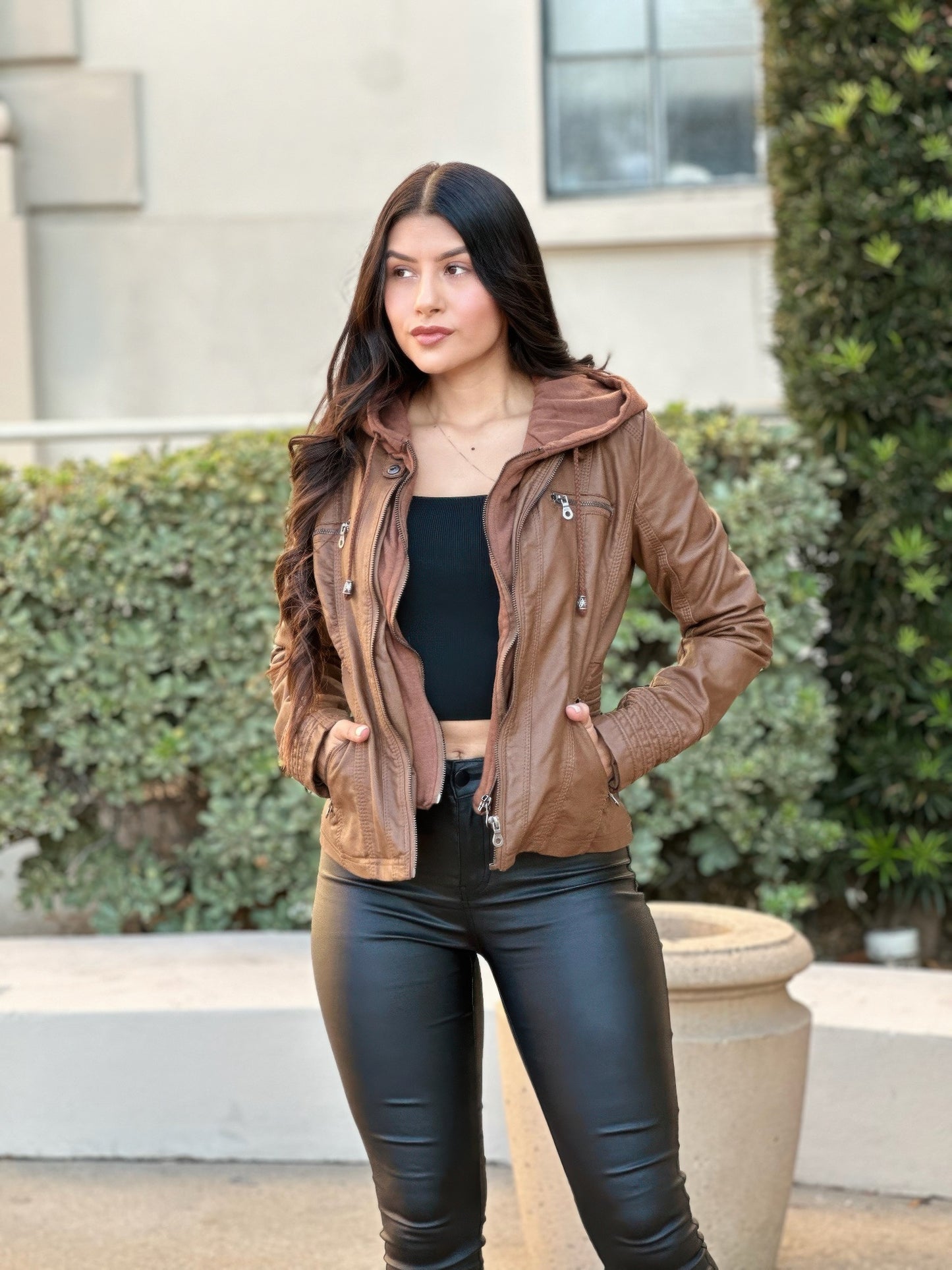 Woman wearing a brown jacket and black pants standing outdoors.