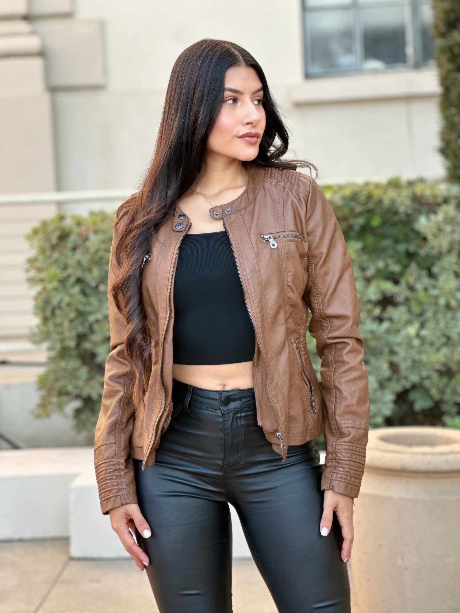 Woman wearing a brown leather jacket and black pants standing outdoors.